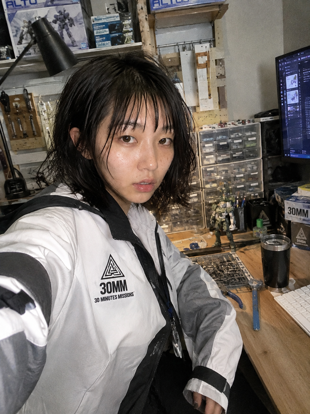生成AIによる案内役キャラクター桐生ここねが、模型棚とPCデスクのある部屋に立っているイラスト
